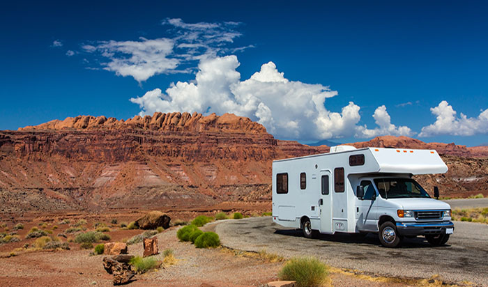 white RV / campervan in canyonlands USA with red cliffs and blue sky behind it