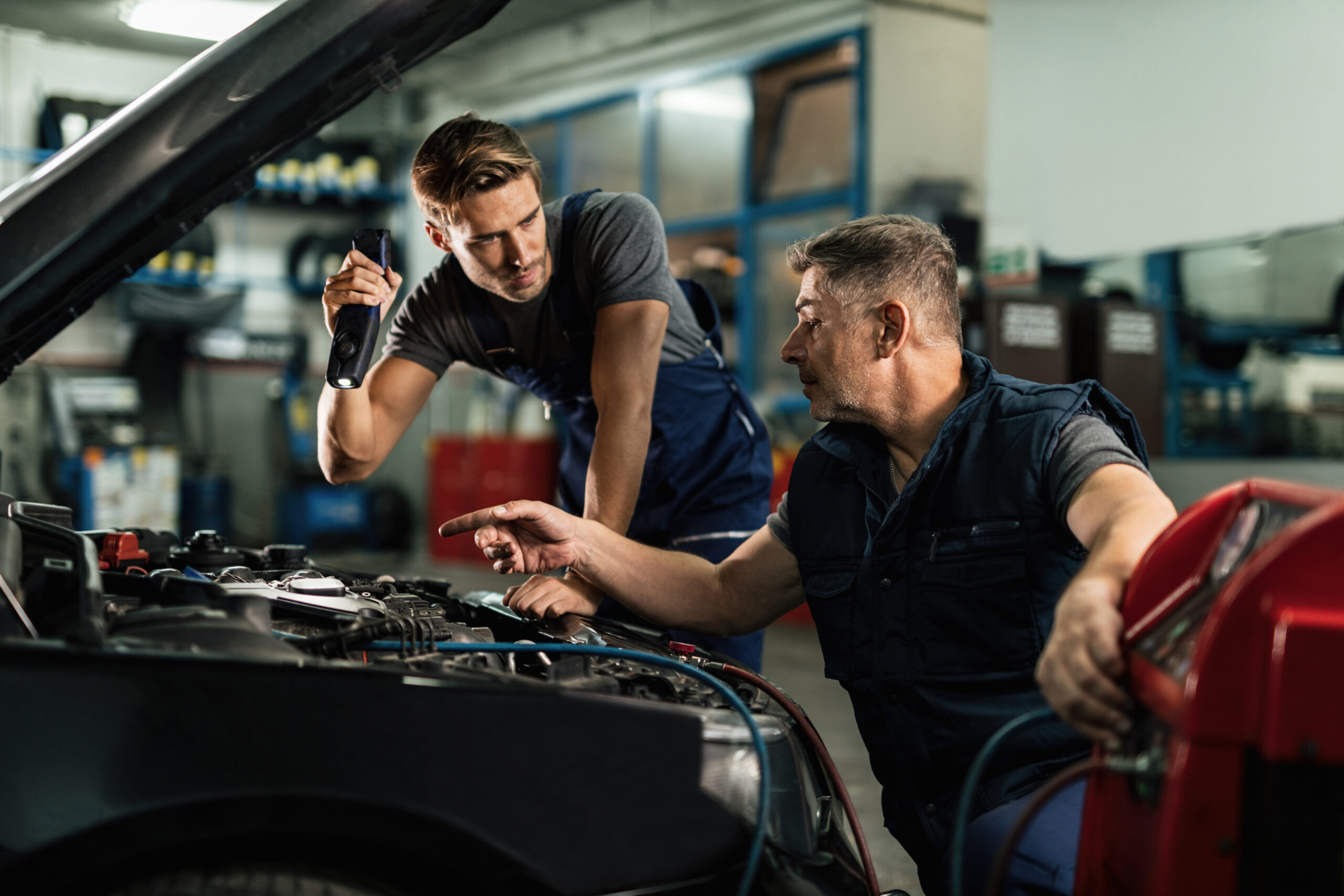 Auto mechanics communicating while doing diagnostic of air conditioning system in a workshop.